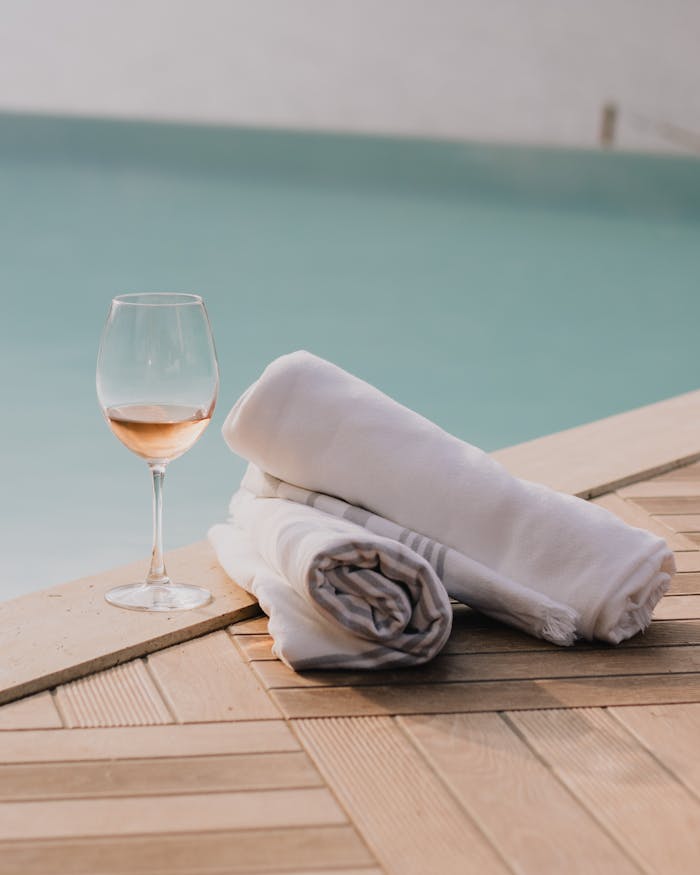 A serene poolside setting with a glass of wine and white towels on a wooden deck.