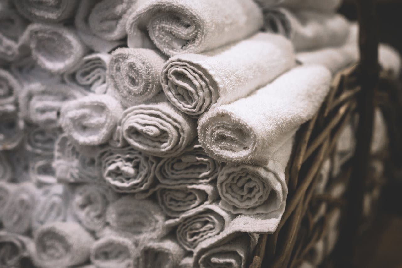 Stack of neatly rolled white towels in a woven basket, perfect for spa or bathroom settings.