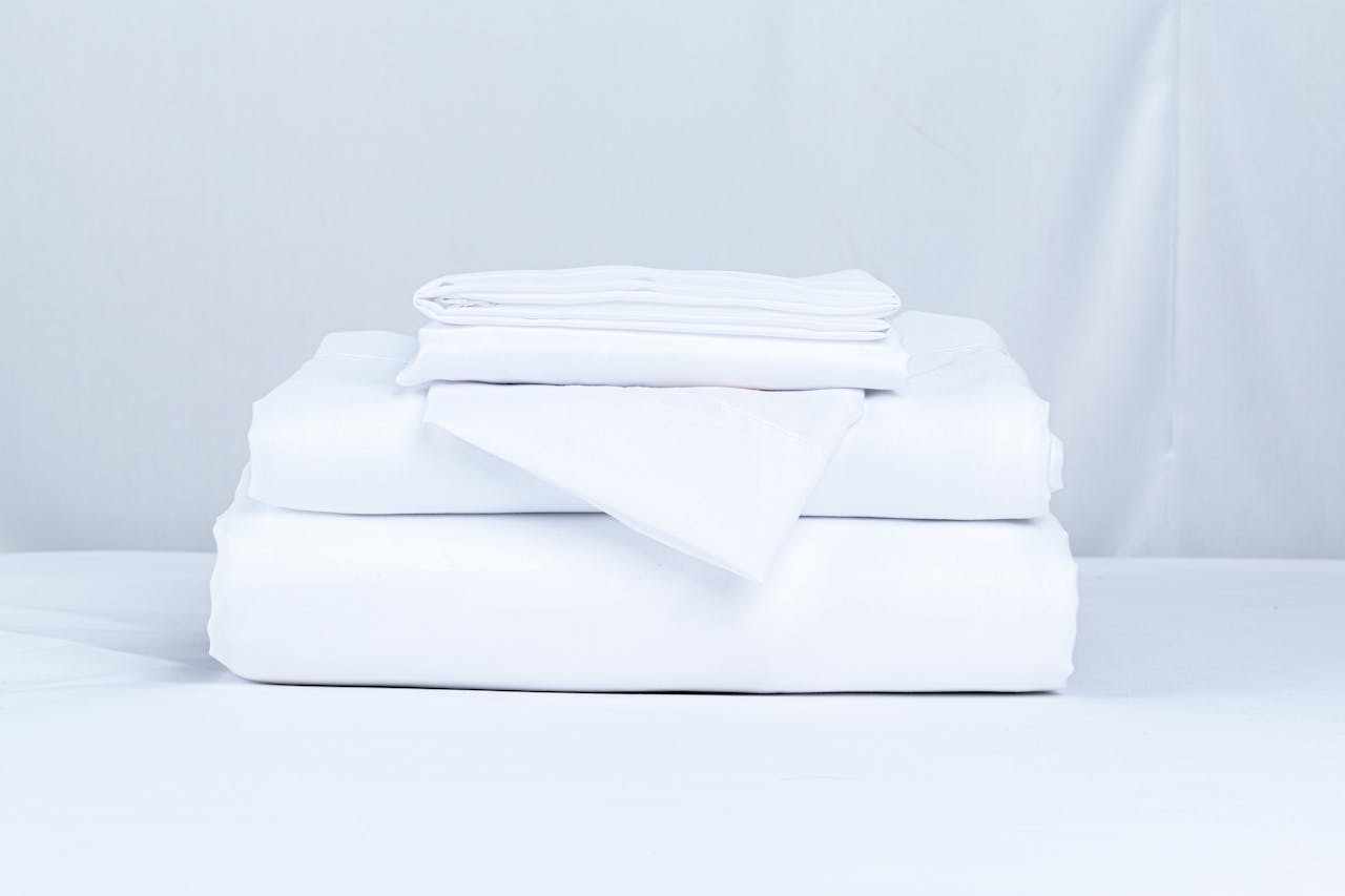 A neatly folded stack of crisp white bed linens on a clean surface.