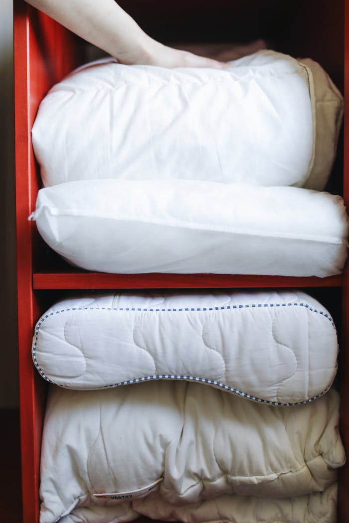A hand adjusting pillows on a neatly organized red shelf, emphasizing home tidiness.